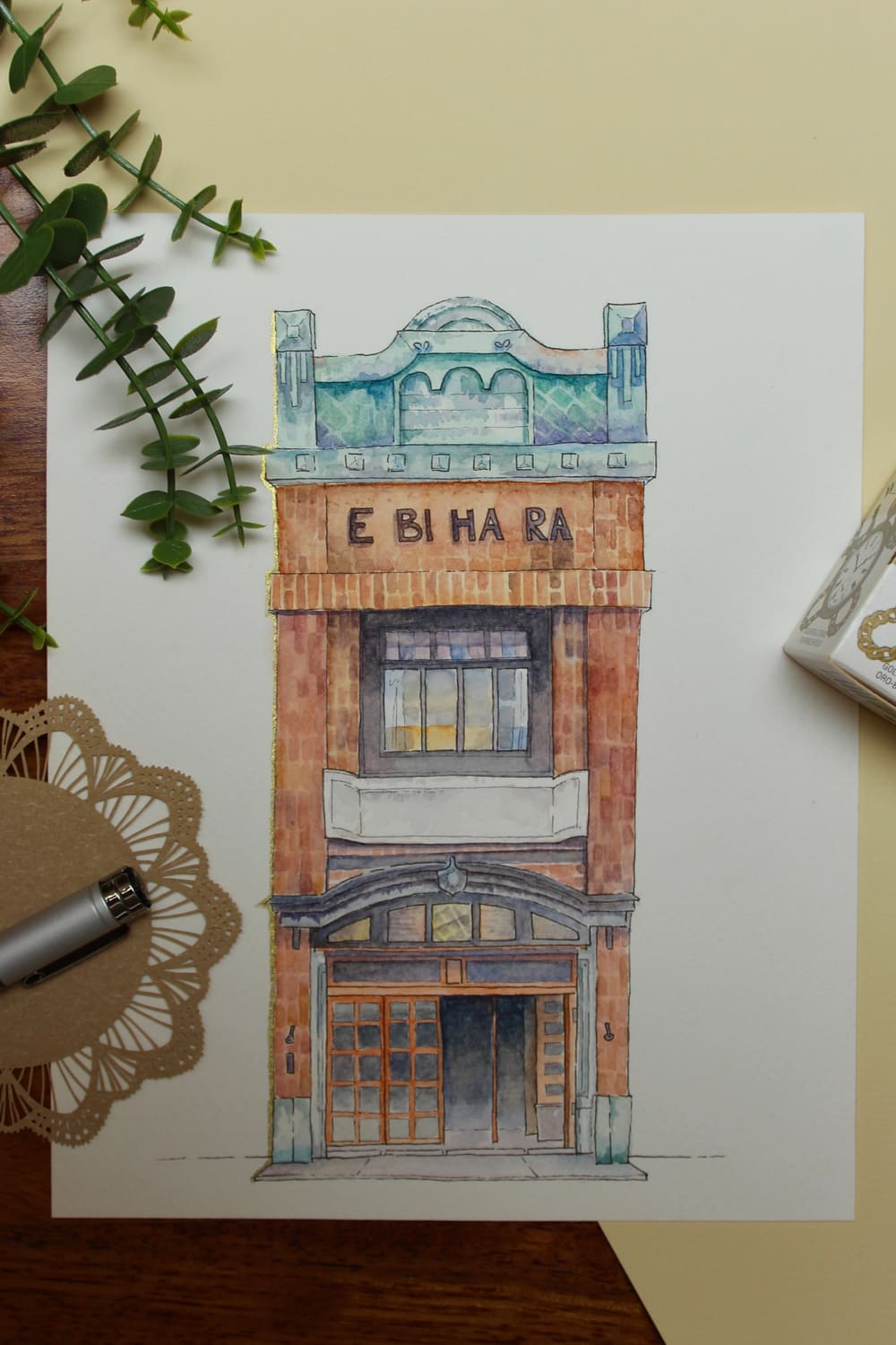 Ebihara, la bottega di mattoni — acquerello di una palazzina stretta in mattoni ocra, con coronamento verderame, l'insegna «E BI HA RA» e un ingresso ad arco in legno arancione.