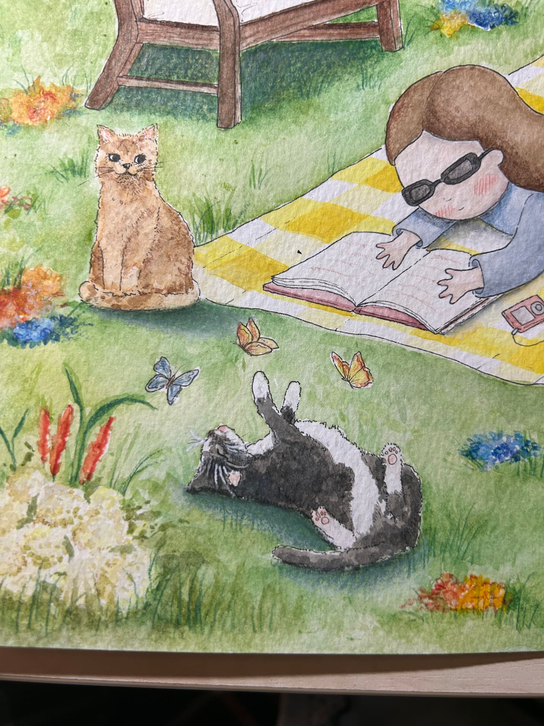 Picnic con i gatti — dettaglio: il gatto rosso seduto nell'erba, il gatto bianco e nero che si rotola a zampe all'aria e le farfalle.