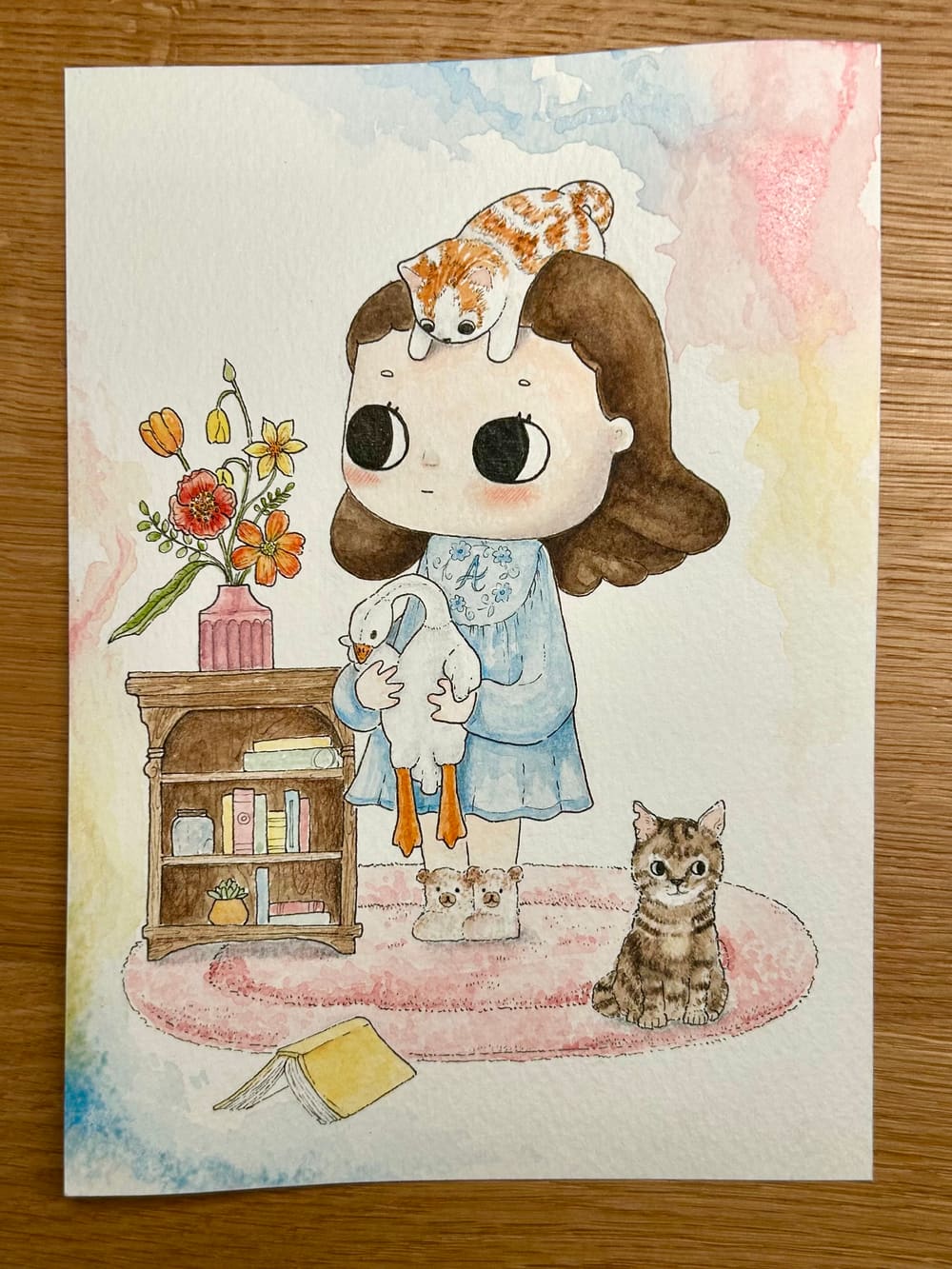 La bambina con l'oca — acquerello su commissione: una bambina in vestitino azzurro stringe un'oca di peluche, con un gattino accucciato sulla testa.
